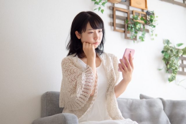 スマホを見つめて悩む女性